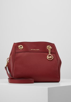 Sac à main en cuir rouge Michael Kors avec chaîne dorée et pendentif logo MK, bandoulière réglable et finition texturée sur une surface blanche.