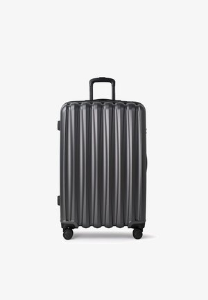 Srebrna walizka twarda z pionowym żebrowanym wzorem, z wysuwaną rączką i czterema obrotowymi kółkami, umożliwiającymi łatwe manewrowanie.