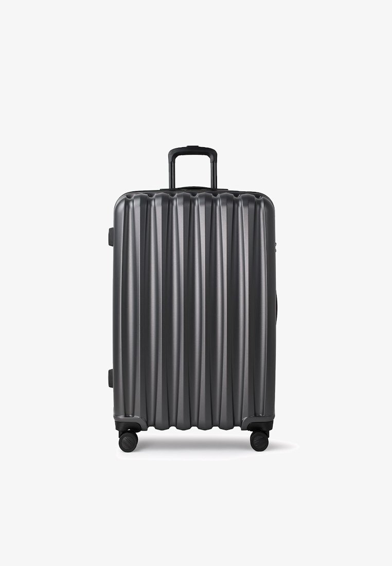 Srebrna walizka twarda z pionowym żebrowanym wzorem, z wysuwaną rączką i czterema obrotowymi kółkami, umożliwiającymi łatwe manewrowanie.