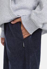 Grå sweatshirt med ribbede manchetter, parret med mørkeblå kordfløjl bukser. Bukserne har sidelommer og et synligt mærkelabel.