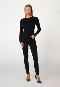 Haut ajusté à manches longues noir avec un léger côtelé au col et aux poignets. Associé à un jean skinny noir et des chaussures à talons hauts.