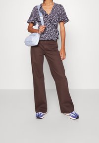 Top avvolgente floreale blu navy con maniche corte, pantaloni larghi marroni, e borsa a tracolla azzurro chiaro abbinata a scarpe da ginnastica blu e bianche.