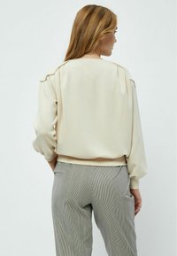 Maglione beige con una vestibilità comoda e maniche a sbuffo, tessuto testurizzato, polsini a coste, abbinato a pantaloni grigi a righe.