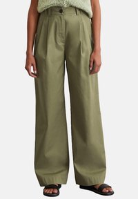 Olijfgroene wijde broek van een lichtgewicht stof met voorplooien en een knoopsluiting. Gedragen met zwarte slip-on sandalen.