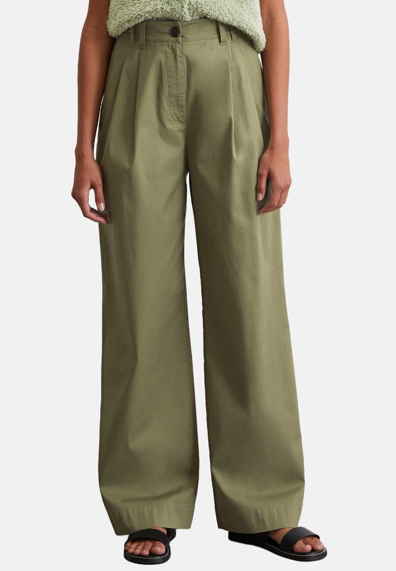 Olijfgroene wijde broek van een lichtgewicht stof met voorplooien en een knoopsluiting. Gedragen met zwarte slip-on sandalen.