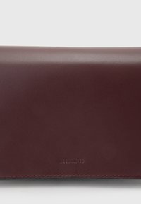 Burgundy läderplånbok med slät yta, med en diskret präglad logotyp och kontrasterande sömmar längs kanterna.