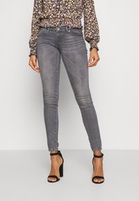 Jeans cinzentos slim feitos de denim, apresentando um design clássico de cinco bolsos com um desgaste subtil. Combinados com uma blusa de padrão floral e saltos pretos.
