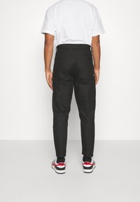 Svarta byxor med en skräddarsydd passform, som har bakfickor och bältesslinga, kombinerat med en vit t-shirt och svarta sneakers.