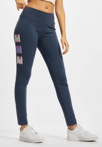 Marineblauwe sportleggings met een hoge tailleband. Heeft drie palmboompjes in roze en paars op het linkerbeen. Voelt glad en rekbaar aan.