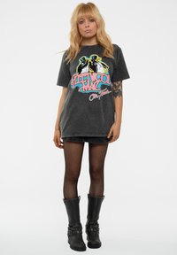 Gray oversized t-shirt with a colorful Fleetwood Mac graphic, worn with a black skirt, black tights, and knee-high black boots with buckles.