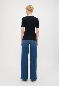Schwarz fitted t-skjorte med korte ermer, kombinert med høyt liv og vide blå jeans som har en klassisk denimtekstur og subtile stitch-detaljer.