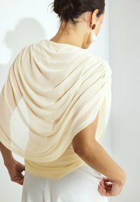 Un tessuto crema trasparente si adagia elegantemente su uno strato di base chiaro, con dettagli arricciati alle spalle e accenti testurizzati.