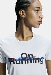 T-shirt blanc avec le texte noir "On Running" et un effet de coup de pinceau coloré en dessous. Manches courtes, col rond, texture lisse.