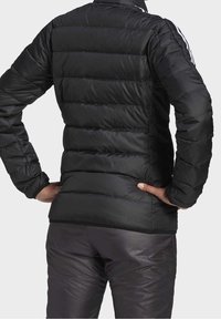 Černá péřová bunda s horizontálními švy a vysokým límcem. Hladká, lesklá textura s bílými pruhy podél rukávů. Kombinov áno s přiléhavými kalhotami.