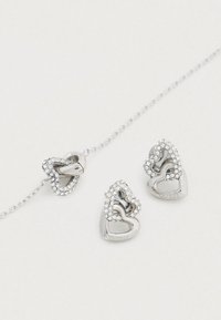 Σετ κοσμημάτων σε σχήμα καρδιάς από ασήμι που περιλαμβάνει κολιέ και σκουλαρίκια με διασταυρούμενα σχέδια καρδιάς και διακοσμημένα με διαφανείς στρας.