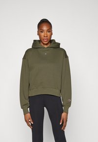 Olivgrüner, kurzer Hoodie mit einem Logo auf der Vorderseite und gerippten Bündchen, kombiniert mit schwarzen Leggings. Weicher, lässiger Stoff, kapuzenförmiges Design.