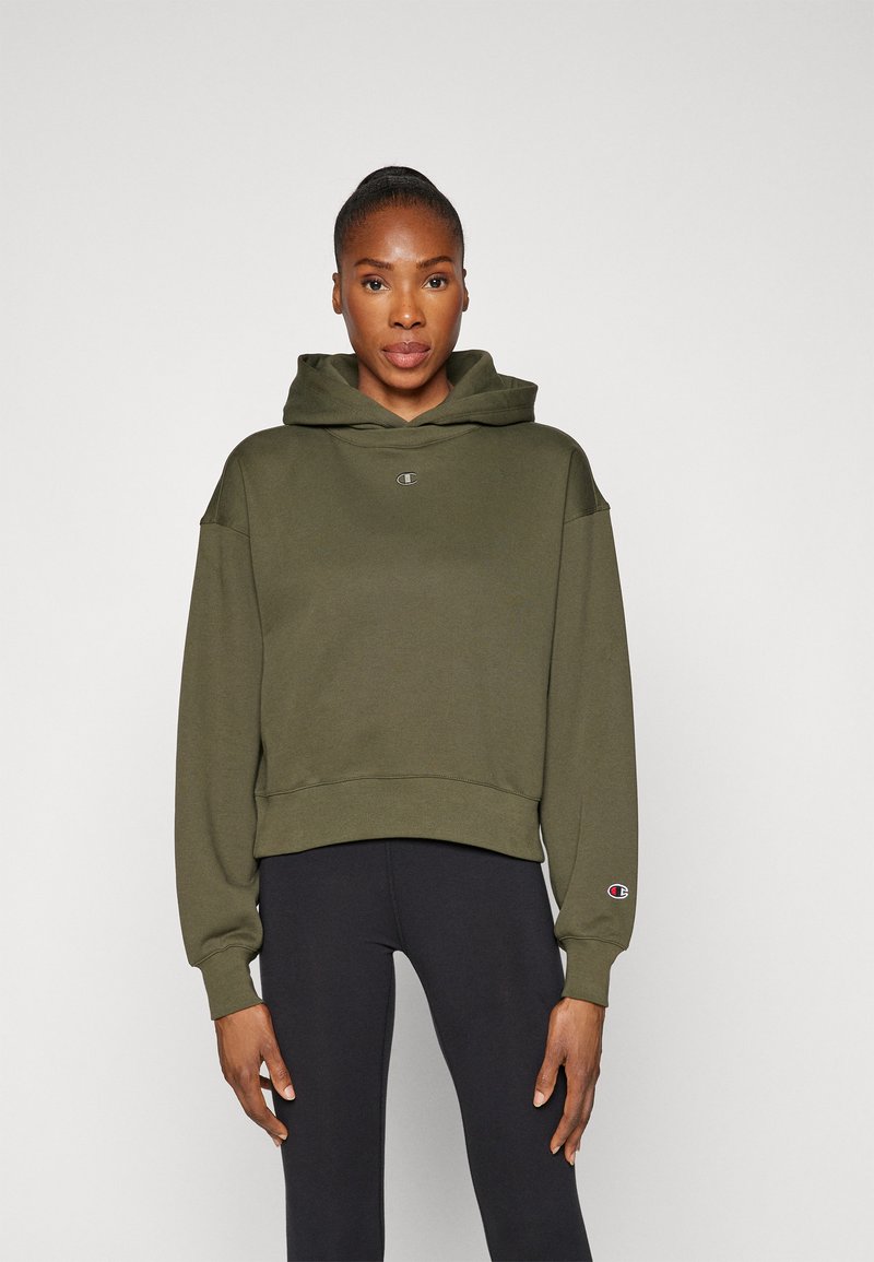Olivgrüner, kurzer Hoodie mit einem Logo auf der Vorderseite und gerippten Bündchen, kombiniert mit schwarzen Leggings. Weicher, lässiger Stoff, kapuzenförmiges Design.
