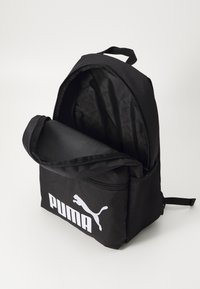 Čierny batoh s hlavným oddelením na zips, predným vreckom s bielym logom Puma, sieťovanými postrannými vreckami a textilnými popruhmi.