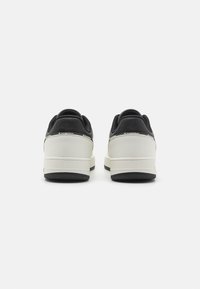 Tenisi alb-negru cu un superior din piele texturată, intermediar alb neted și talpă din cauciuc negru. Proiectați pentru un aspect casual cu un stil minimalist.