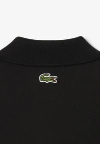 Col polo noir avec un col en tissu texturé. Présente un logo de crocodile brodé en vert sur le côté gauche.