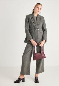 Sivi houndstooth blejzer s remenom, odgovarajuće široke hlače, lakirane burgundske mule i mala burgundska torbica.