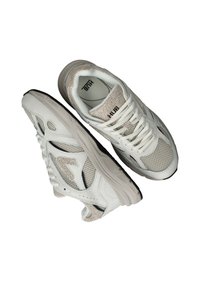 White athletic sneakers with mesh panels and textured accents. Padded tongue and collar, featuring a black rubber sole and discreet logo.