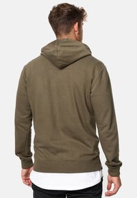 Sweat à capuche en vert olive, fabriqué en coton doux. Il présente des manches longues, des poignets côtelés et une poche kangourou à l'avant.