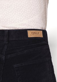 Tmavě modré kordové kalhoty s texturovaným povrchem, s koženou etiketou s nápisem "ONLY" na pase, stylizované se zadními kapsami.