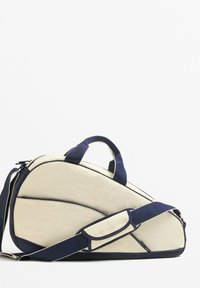 Valkoinen ja laivastonsininen urheilulaukku, jossa on kaareva muotoilu ja joka on valmistettu tekstuurillisesta kankaasta. Laukussa on kaksi kahvaa ja irrotettava olkahihna monipuolista kantamista varten.