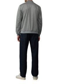 Szary sweatshirt o teksturowanym wykończeniu, z ściągaczami przy mankietach i w pasie, w połączeniu z ciemnymi dżinsami i białymi trampkami.