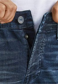 Mörkblå denimjeans med en slät yta, med en metallknappstängning och synliga sömmar längs midjebandet.