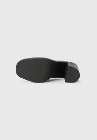 Semelle de chaussure en cuir noir avec une finition lisse et texturée, de forme arrondie et un design de talon modéré. Pas de motifs ou d'accents distincts.