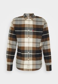 Camicia di flanella a quadri nei toni del marrone, nero e crema. Design con bottoni e taschino sul petto con una piccola targhetta logo.