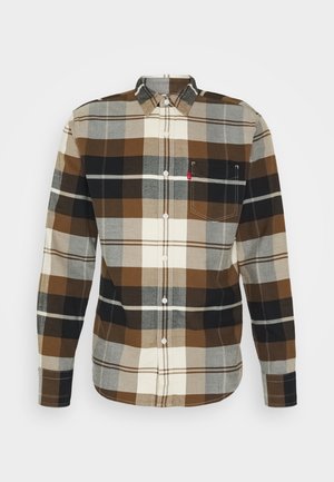 Camisa de franela de cuadros en tonos marrón, negro y crema. Diseño abotonado con un bolsillo en el pecho y una pequeña etiqueta con logo en el bolsillo.