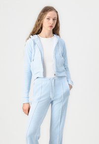 Lichtblauwe zip-up hoodie met trekkoorden en zakken aan de voorkant, gecombineerd met bijpassende lichtblauwe joggers met details van zijpiping.