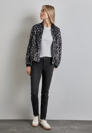 Veste bomber en imprimé léopard gris et noir, associée à un haut blanc, un jean noir et des baskets blanches. Tissu doux et texturé avec des poignets élastiques.