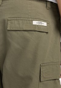 Bermudas cargo en verde olivo con una tela texturizada, que cuentan con un bolsillo trasero con parche y una etiqueta de Element Skateboard Co.