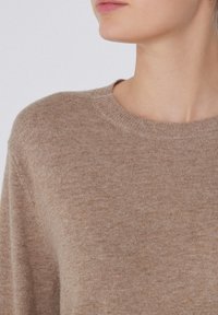 Beige Strickpullover mit rundem Ausschnitt und gerippten Bündchen, der eine weiche Textur und ein dezentes meliertes Muster aufweist.