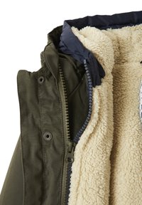 Grüne Jacke mit marineblauem Kragen und cremefarbenem, flauschigem Fleece-Futter, ausgestattet mit einem Reißverschluss und Druckknöpfen auf der Vorderseite.