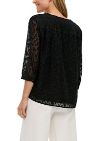 Zwarte doorzichtige blouse met een luipaardprint, driekwartmouwen en rimpeldetails op de rug. Licht en luchtig materiaal.