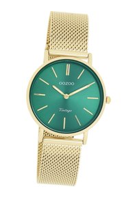 Montre en métal vert avec un bracelet en mailles dorées, design minimaliste, cadran rond, index des heures dorés, et le détail textuel "Vintage" sur le cadran.