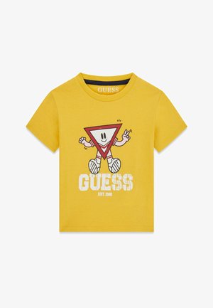 Žuto majica kratkih rukava s crvenim likom crtane trokuta koji pokazuje znak mira, bijeli tekst "GUESS EST. 1981" ispod lika.