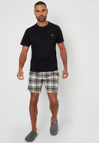 Sort kortærmet skjorte, ternede shorts i beige og sort, samt grå slip-on sko. Uformel outfit med enkelt design og bløde teksturer.
