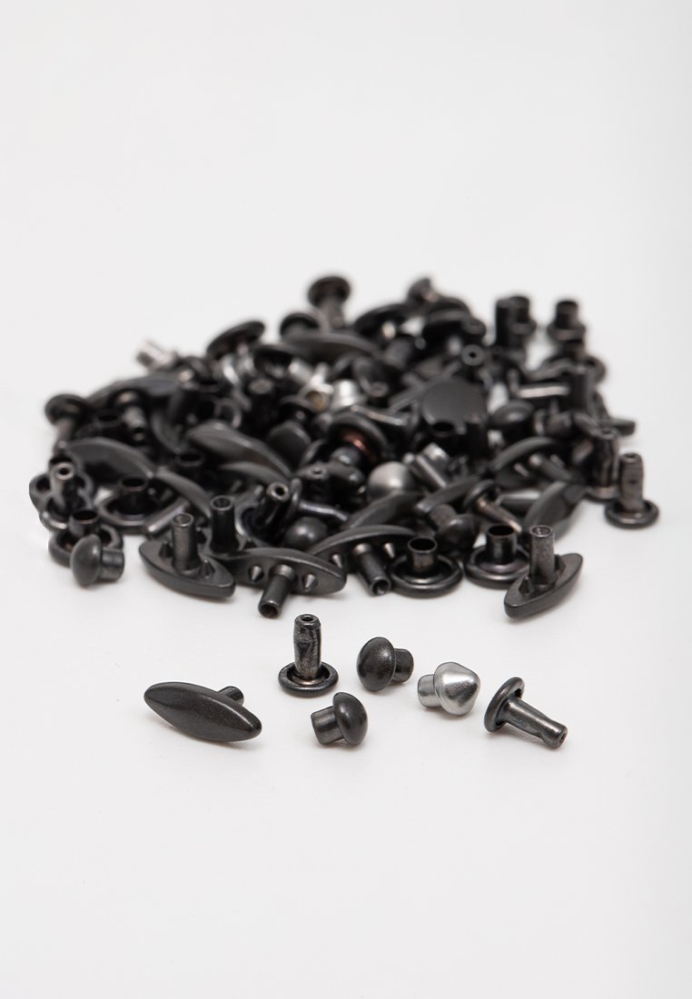 Schwarze Metallbeschläge in verschiedenen Formen und Größen, darunter runde und ovale Köpfe, auf einem weißen Hintergrund verstreut.