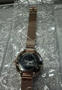 Roségoldfarbene Edelstahl-Uhr mit Mesh-Armband, rundem Gehäuse und schwarzem Zifferblatt mit weißem Text. Wasserdicht, in Luftpolsterfolie verpackt.