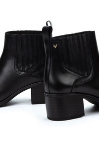 Botas de tobillo de cuero negro con tacones de bloque, paneles laterales elásticos y un pequeño logo dorado en el lado exterior.