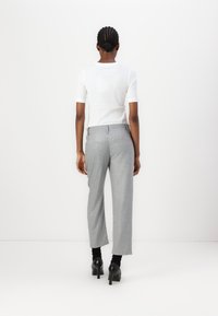 Weißes kurzärmliges Hemd, graue weite Hose mit strukturiertem Muster und schwarze High Heels, von hinten betrachtet.