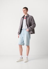 Veste en velours côtelé grise, t-shirt gris clair avec accent rouge, shorts en denim bleu clair, baskets blanches, portées avec des chaussettes blanches.