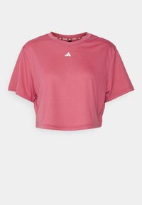 Krótki top w stonowanym różowym kolorze, wykonany z miękkiego materiału. Posiada okrągły dekolt i krótkie rękawy, z małym białym logo na piersi.