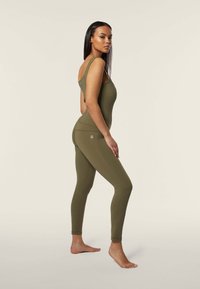 Body verde oliva con scollatura a barca e design a spalla singola, abbinato a leggings aderenti coordinati. Texture liscia con cuciture minime.